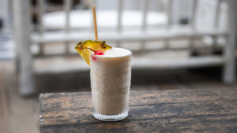 A glass of piña colada garnished with pineapple and cherry on a wooden table