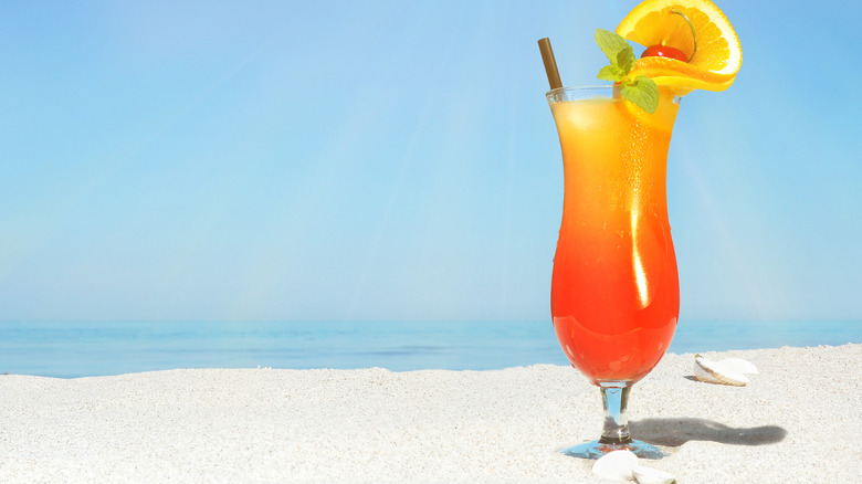 Sex on the beach cocktail on a sandy beach garnished with orange, mint, and a cherry