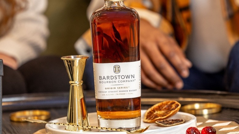 A bottle of Bardstown Bourbon Company shown on a serving tray next to cocktail accessories and ingredients.