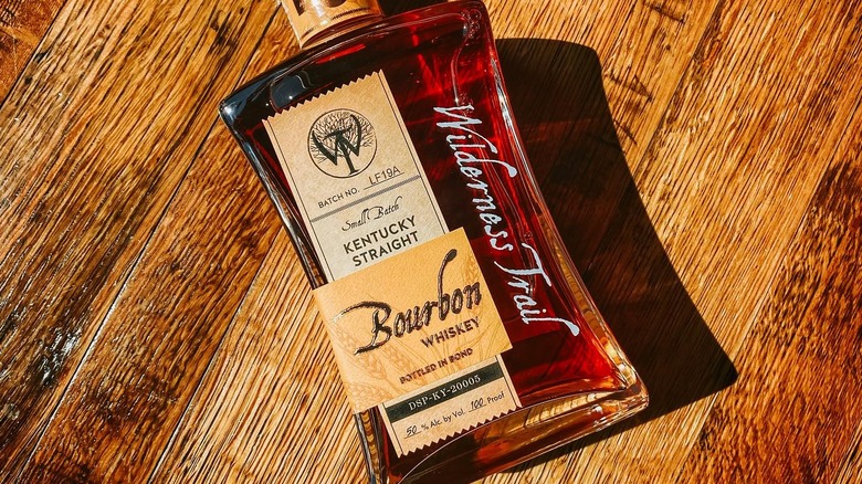 A  bottle of Wilderness Trail Bourbon laid on a wooden surface while being bathed in sunshine