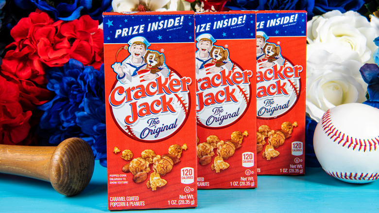 Cracker Jack snack boxes on table beside baseball bat, baseball, and colorful flowers