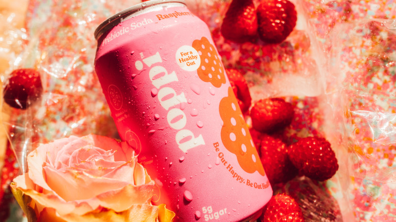 Poppi probiotic canned soda beside raspberries and flowers