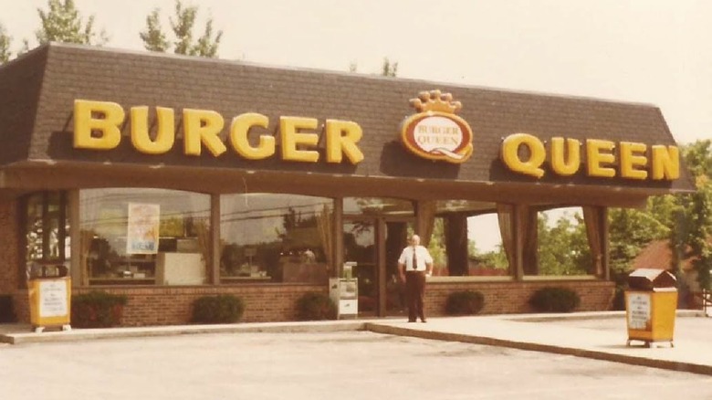 a grainy image of an old Burger Queen restaurant with a man in a shirt and tie outside