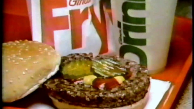 Grainy image of a close up burger from Gino's Hamburgers with drinks behind