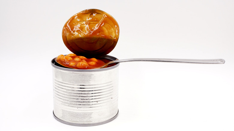 An open can of baked beans with a spoon resting on top, with a white background.