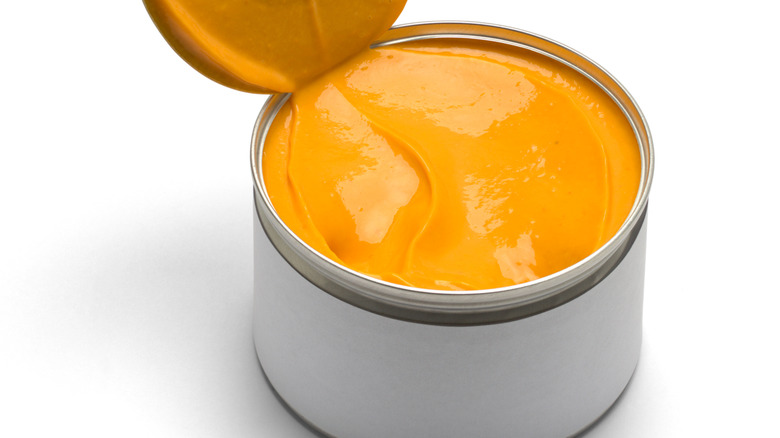 An opened can of orange cheese sauce with a white background.