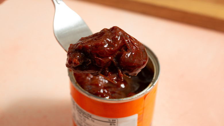 A fork holding up a scoop of chipotle peppers in adobo sauce from a can on a countertop.
