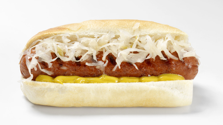A hot dog with sauerkraut and yellow mustard, with a white background.
