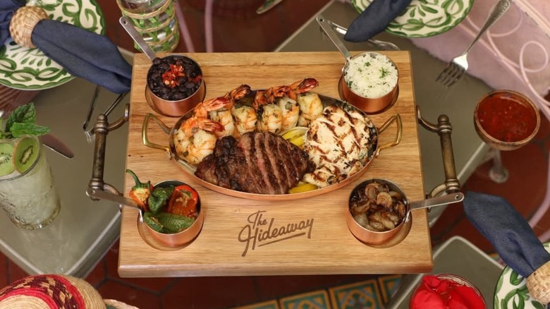 Shrimp, steak, chicken, and rice on wooden board carved with The Hideaway logo