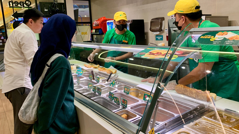 Customers getting their sandwiches at a Subway assembly line
