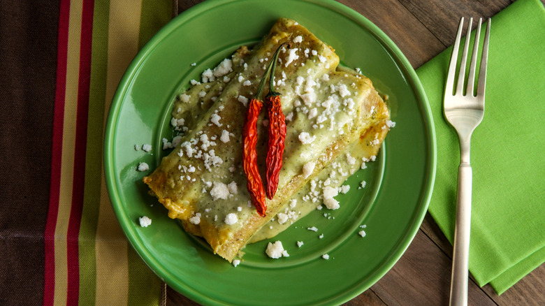 Enchiladas verdes on a green plate with a fork beside it