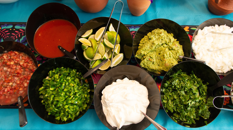 Salsa bar with dips and toppings in black bowls on a blue table