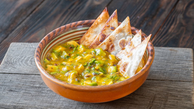 Mango avocado salsa with triangle chips resting in a clay bowl