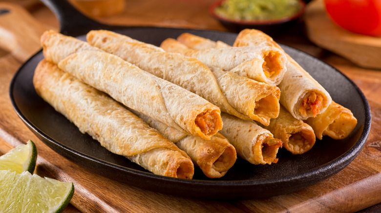 Pile of taquitos on a black bowl resting on a wooden cutting board