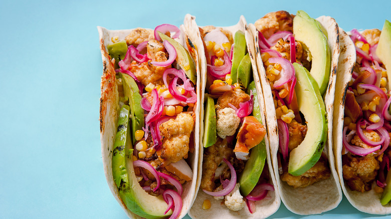Four cauliflower tacos with avocado and red onion against a blue background