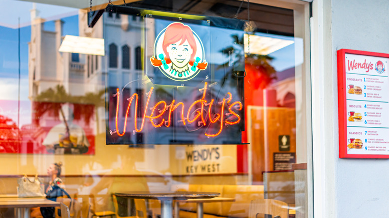 Wendy's neon sign in a window with tables in the background