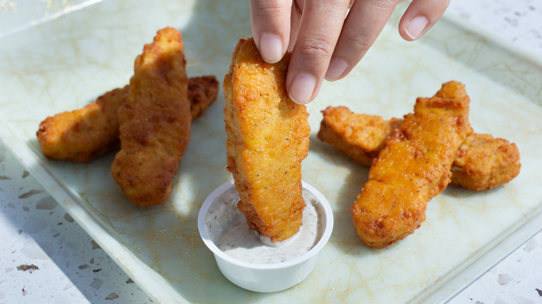 Plant-based chicken tenders being dipped into ranch by a hand