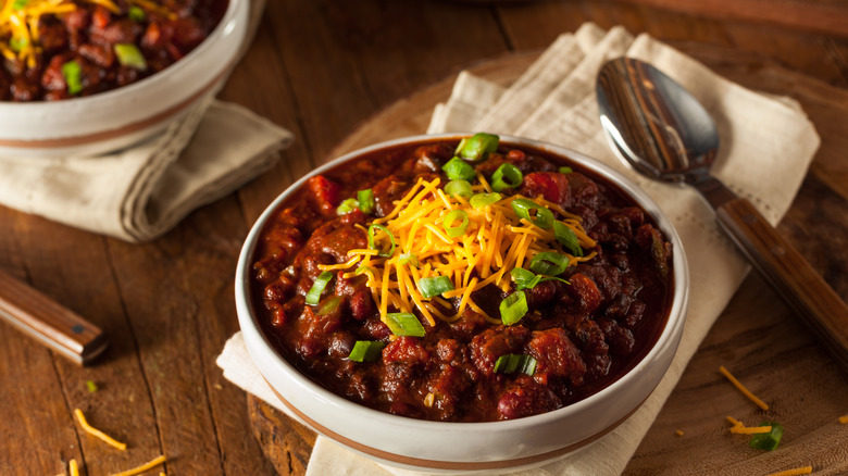 Vegetarian chili with cheese and green onions on top of a wooden table