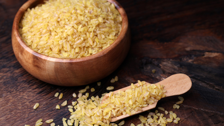 A wooden bowl full of bulgur wheat grains with more on a wooden spoon next to it
