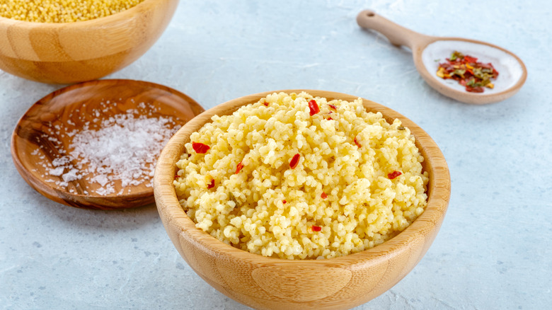 A wooden bowl of cooked millet with a small dish of salt nearby