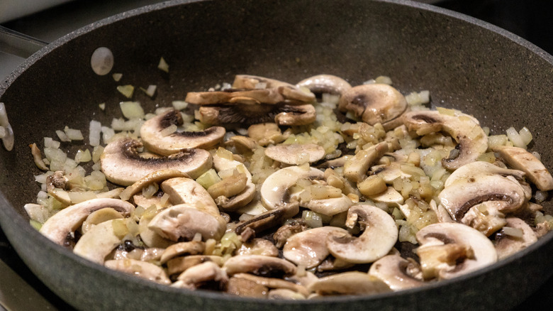 A pan of mushrooms being fried with some onions