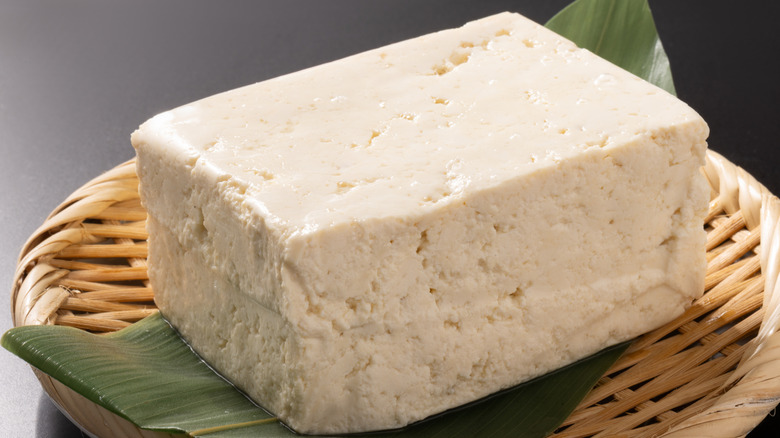 A block of extra firm tofu sitting on a banana leaf in a wicker bowl