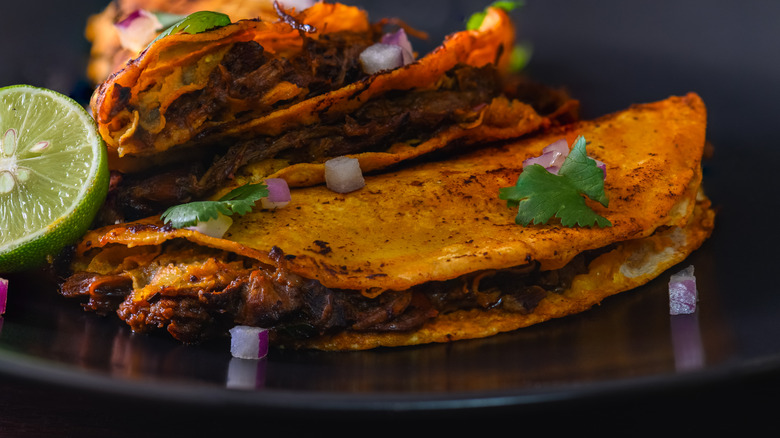 Crispy birria tacos with a lime on a black plate