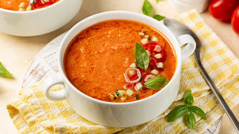 A white bowl of tomato gazpacho on a yellow checked table cloth