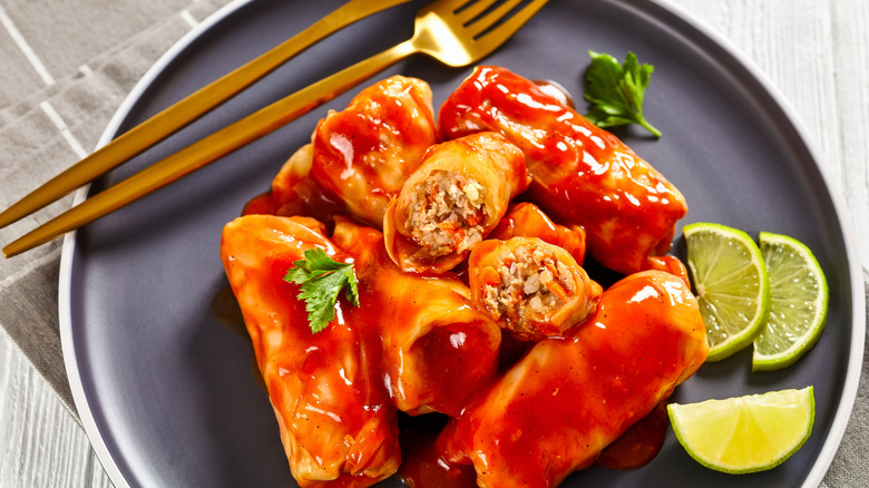 A plate of golabki cabbage rolls with a lime and a knife and fork