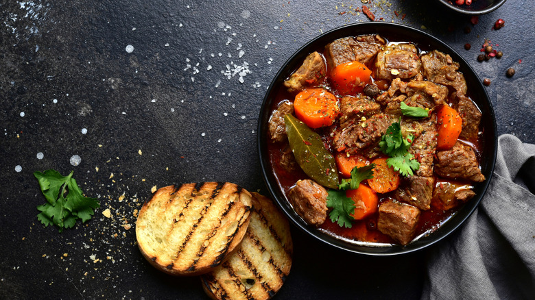 A black pot of goulash with garlic bread
