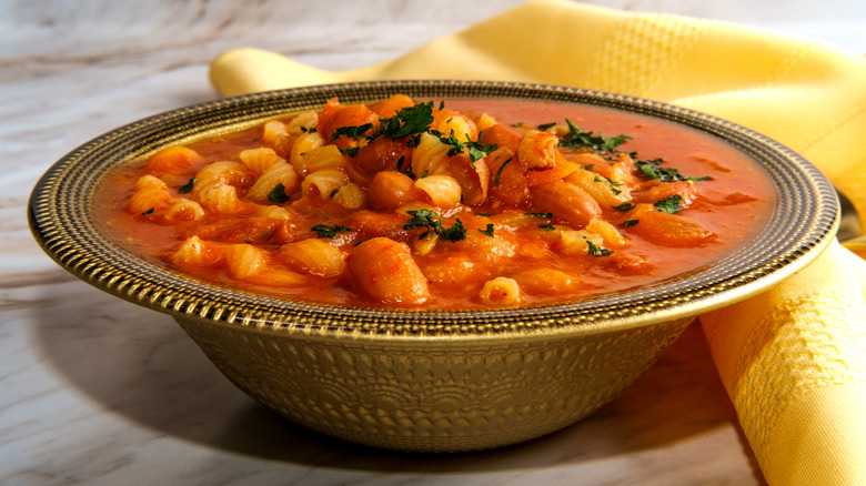 A metal dish of Pasta e fagioli next to a yellow table cloth