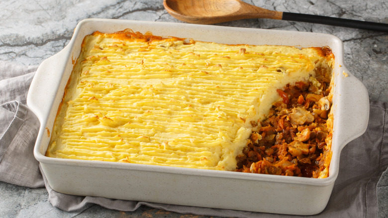A dish of shepherd's pie next to a wooden spoon