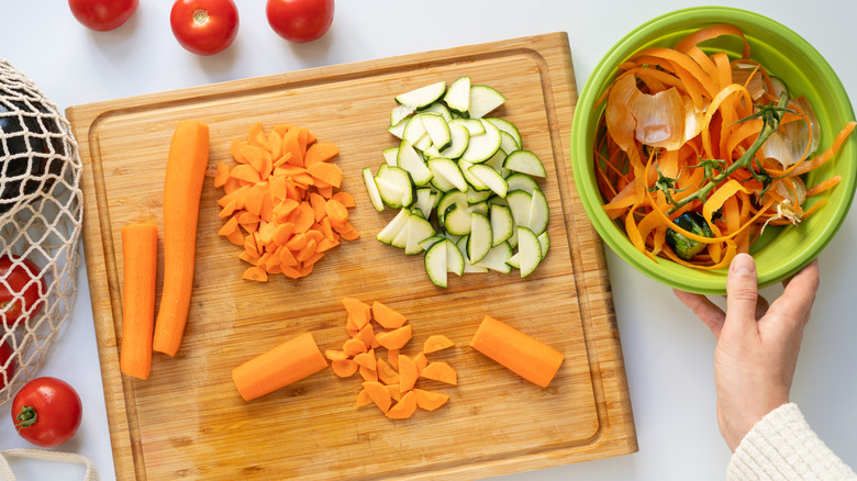 Person preparing vegetables with scrap bowl near cutting board