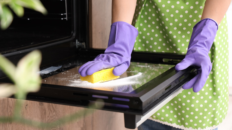 Person in purple gloves sponging oven door