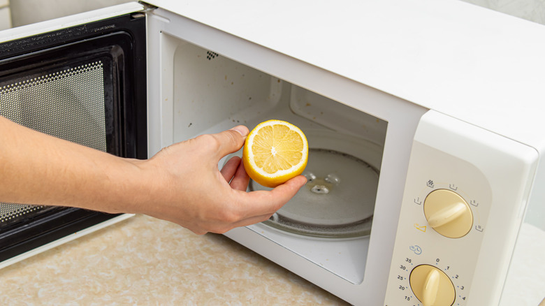 Hand putting lemon in microwave