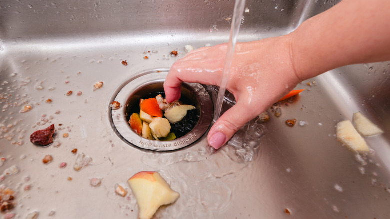 Hand pushing food scraps into sink garbage disposal