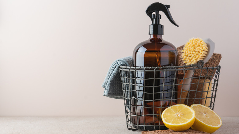 Bottling of cleaning spray in metal basket with scrubber, next to fresh halved lemon