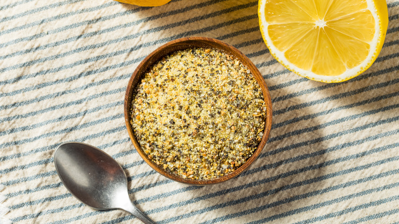 Bowl of lemon pepper seasoning next to spoon and fresh, halved lemon