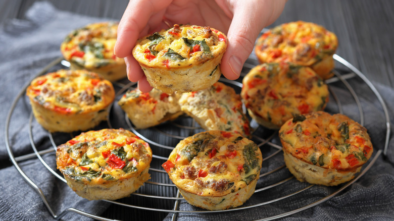 Vegetable muffins on wire cooling rack with hand picking one muffin up