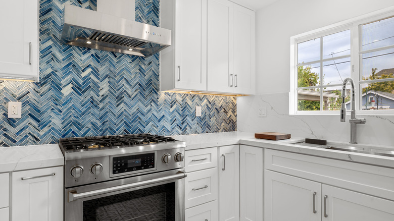 Contemporary kitchen with blue tiled backsplash against white cabinetry