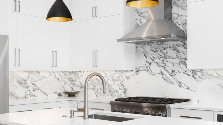 All-white kitchen with marble backsplash, white cabinets and modern light fixtures