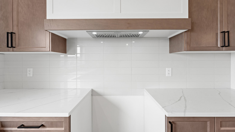 Empty kitchen with tiled backsplash under brown cabinets