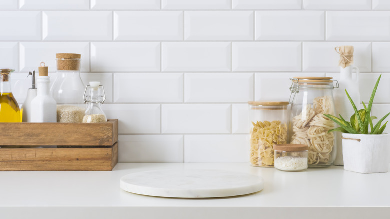 All-white kitchen with cooking essentials in jars placed against tiled backsplash