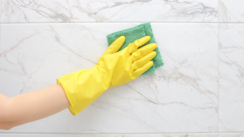 Hand wearing yellow gloves cleaning marble tiles with a green cloth