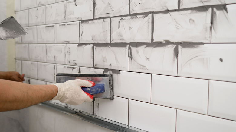 Hand applying grout to white ceramic tiles
