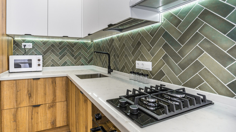 Kitchen with green tiled backsplash above white countertops