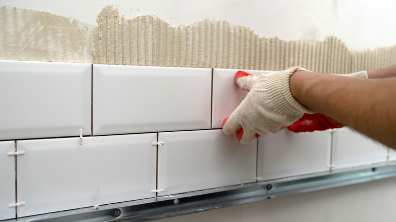 A pair of hands laying down ceramic tiles on the kitchen backsplash
