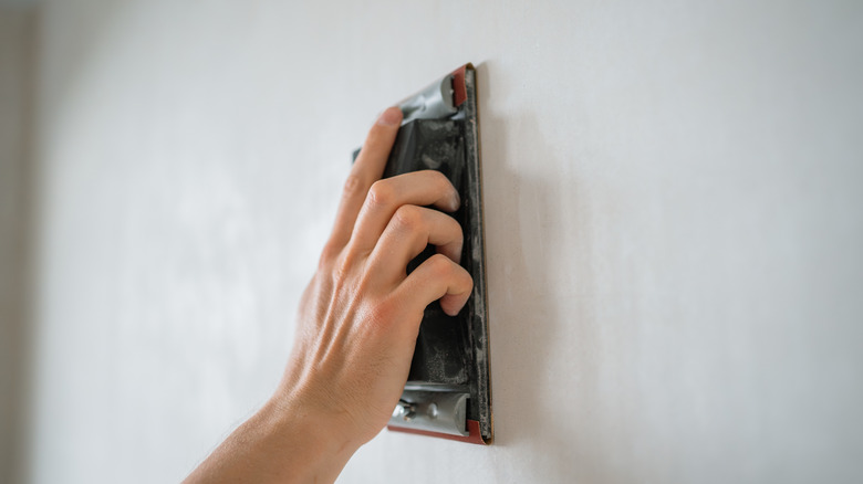 Hand using sandpaper on a white wall to create a smooth surface
