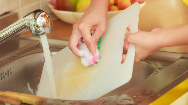 person washing scratched plastic cutting board