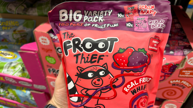 A person holding a variety package of Froot Thief Fruit Whips inside a Costco store